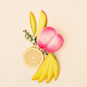May include: A still life arrangement of fresh fruit on a light peach background. The composition includes slices of yellow mango, a halved lemon, a pink peach, and small white flowers.