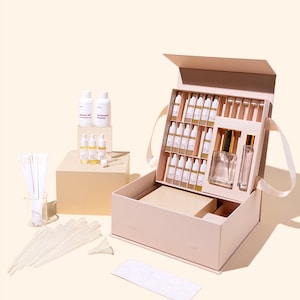 May include: A pink perfume making kit with a variety of vials, bottles, and accessories. The kit includes a large box with multiple small vials, two spray bottles, and other supplies. There are also bottles of coconut oil and perfumer's alcohol.