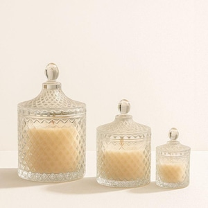 May include: Three clear glass candles with diamond-patterned jars and matching lids. The candles are different sizes, with a light-colored wax inside. Each candle has a wick visible at the top.