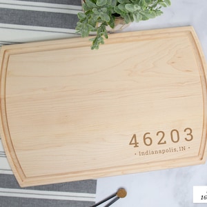 May include: A natural wood cutting board with rounded edges. The board is made of maple and measures 16 inches by 10.5 inches. The board is engraved with the text "46203 Indianapolis, IN".