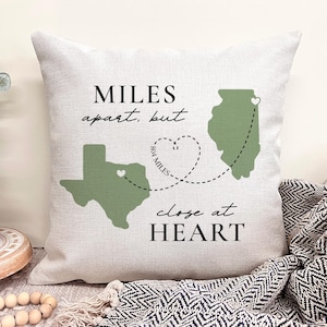 May include: A decorative pillow with the text "MILES apart, but close at HEART." The pillow features green outlines of the states of Texas and Illinois, connected by a dotted line and a heart, with the distance of 804 miles.