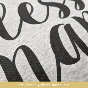 May include: Close-up of a gray fabric with large, black cursive lettering. The fabric has a textured appearance. The bottom of the image includes the text: "Eco-Friendly, Water-Based Inks."