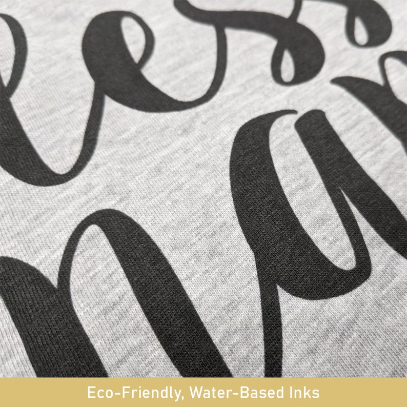 May include: Close-up of a gray fabric with large, black cursive lettering. The fabric has a textured appearance. The bottom of the image includes the text: "Eco-Friendly, Water-Based Inks."