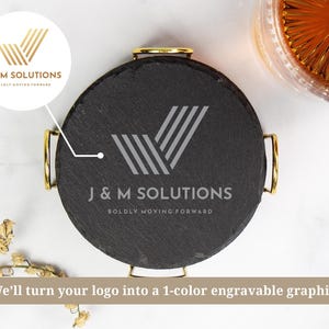 以下が含まれることがあります： 金色のハンドルが付いた丸い黒いスレートコースター。シルバーの「J＆M SOLUTIONS」のロゴと「BOLDLY MOVING FORWARD」の文字が表示されています。琥珀色の液体が入ったグラスとドライフラワーも画像に表示されています。