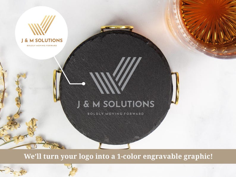 以下が含まれることがあります： 金色のハンドルが付いた丸い黒いスレートコースター。シルバーの「J＆M SOLUTIONS」のロゴと「BOLDLY MOVING FORWARD」の文字が表示されています。琥珀色の液体が入ったグラスとドライフラワーも画像に表示されています。