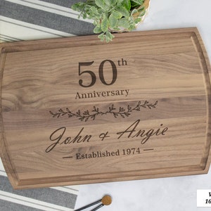 May include: Walnut cutting board with a 50th anniversary inscription, the names John & Angie, and the year 1974. The board measures 16 inches by 10.5 inches.