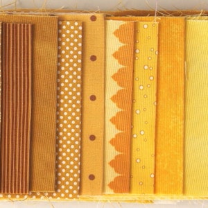 Könnte beinhalten: Eine Sammlung von 10 Stoffstreifen in verschiedenen Gelb- und Brauntönen. Die Stoffstreifen haben unterschiedliche Muster, darunter Punkte, Streifen und ein Blumenmuster.