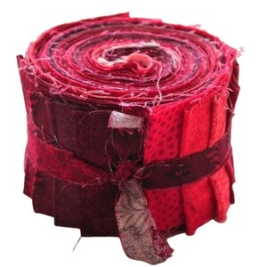 Könnte beinhalten: Eine Rolle mit roten und rosafarbenen Stoffresten, gebunden mit einem passenden Stoffband. Die Stoffreste sind spiralförmig angeordnet und bilden ein farbenfrohes und strukturiertes Design.