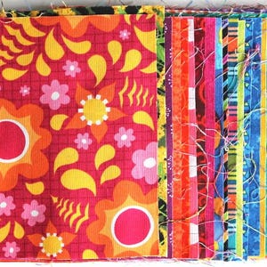 Könnte beinhalten: Ein Stapel bunter Stoffquadrate mit verschiedenen Mustern, darunter florale, geometrische und gestreifte Designs. Das oberste Quadrat hat einen leuchtend roten Hintergrund mit orangefarbenen und gelben Blumen.