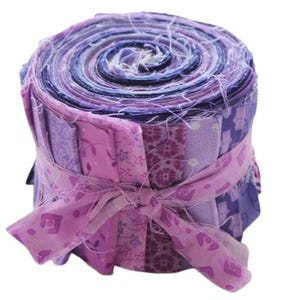 Könnte beinhalten: Eine Rolle mit violetten und rosafarbenen Stoffresten, die mit einem passenden Band zusammengebunden sind. Die Stoffreste sind spiralförmig angeordnet und eignen sich perfekt zum Quilten oder für andere Bastelprojekte.