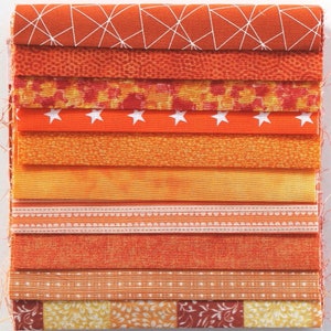 Könnte beinhalten: Ein Stapel aus 10 orangefarbenen Stoffstreifen mit verschiedenen Mustern, darunter geometrische Muster, Sterne und Blumenmuster.