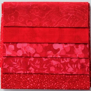 Könnte beinhalten: Ein Stapel roter Stoffquadrate, jedes mit einem anderen Muster. Die Muster umfassen Wirbel, unifarbene Farben, florale Designs und eine gepunktete Textur. Die Stoffe sind ordentlich gestapelt und zeigen eine Vielzahl von Rottönen.