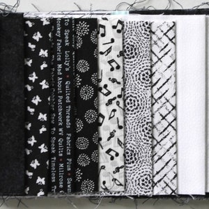 Könnte beinhalten: Eine Sammlung von schwarzen und weißen Stoffstreifen mit verschiedenen Mustern, darunter Noten, Punkte und geometrische Muster. Die Stoffstreifen sind mit den Namen von Stoffgeschäften und Quiltmarken beschriftet, darunter "Quilted Threads Fabrics Plus Sawmill Creek", "Monkey Fabrics Mad About Patchwork WV Quilts Millrose" und "The Fabric Cobbler Sew To Speak Timeless Treasures".