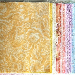 Könnte beinhalten: Ein Stapel Stoffquadrate mit verschiedenen Mustern und Farben. Das oberste Quadrat ist ein gelber Stoff mit einem weißen Blumenmuster.