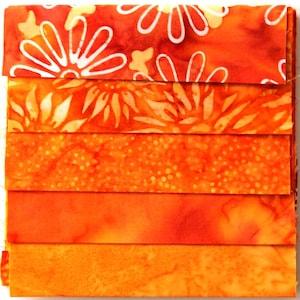 Könnte beinhalten: Ein Stapel orangefarbener Stoffstreifen mit verschiedenen Mustern. Der oberste Streifen zeigt große weiße Blumenmuster. Andere Streifen umfassen Blumen-, gepunktete und unifarbene orangefarbene Muster. Die Stoffe sind wahrscheinlich für Quilt- oder andere Bastelprojekte bestimmt.