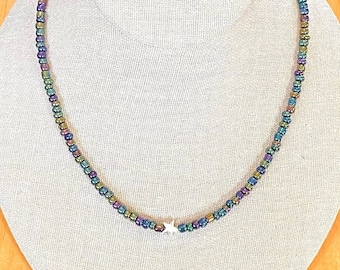 May include: A silver star charm hangs from a delicate necklace made of iridescent beads in shades of green, blue, and purple.