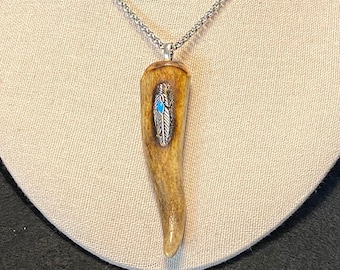 May include: A silver chain necklace with a pendant made from a brown antler with a silver feather design and a turquoise stone.