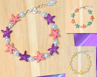 Puede incluir: Tres pulseras con diseño de estrella de mar. La primera pulsera tiene cuentas de estrella de mar moradas, rosadas y blancas. La segunda pulsera tiene cuentas de estrella de mar verdes, naranjas y blancas. La tercera pulsera tiene cuentas de estrella de mar amarillas, blancas y naranjas.