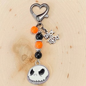 May include: A silver keychain with a heart-shaped clasp, black and orange beads, a silver charm that says "Trick or Treat", and a silver charm with a white Jack Skellington face.