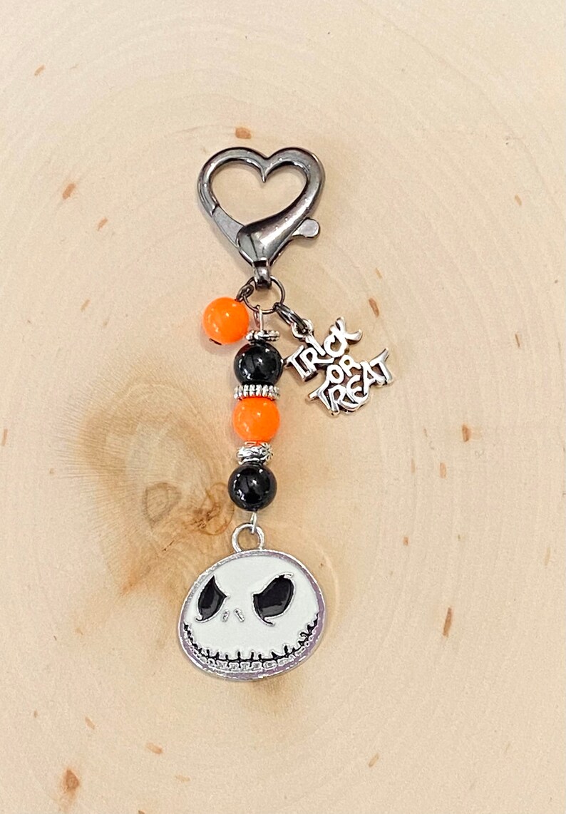 May include: A silver keychain with a heart-shaped clasp, black and orange beads, a silver charm that says "Trick or Treat", and a silver charm with a white Jack Skellington face.
