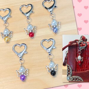 May include: Five silver heart-shaped keychains with angel charms. Each charm features a white pearl, a smaller pearl, and a colored pearl in red, purple, blue, yellow, or black.