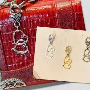 May include: Three silver-toned heart-shaped zipper pulls with a decorative design. The zipper pulls are on a wooden surface.