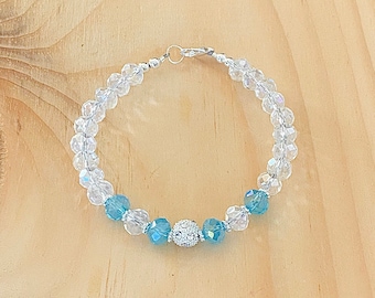 May include: A silver bracelet featuring clear and light blue crystal beads. The bracelet has a silver clasp and a larger, sparkly, light blue bead in the centre.