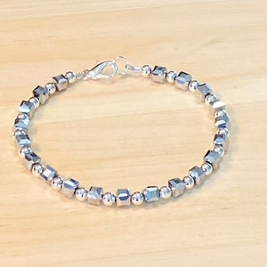 Puede incluir: Un brazalete plateado con un cierre plateado y cuentas cuadradas.