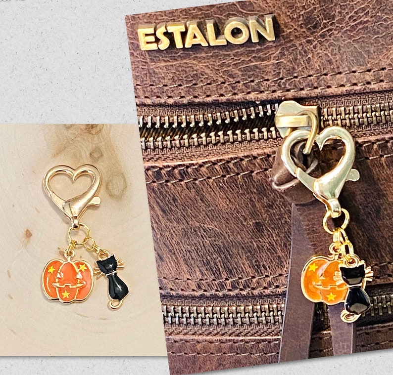 May include: Gold-tone pumpkin and black cat charm with a heart-shaped clasp. The charm is attached to a brown leather bag with the word "ESTALON" embossed on the front.