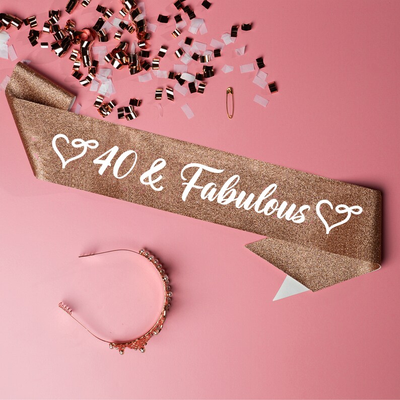 May include: A gold glitter sash with the text "40 & Fabulous" in white lettering and a heart design on each end. A gold headband with rhinestones is also pictured.