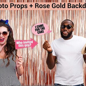 Op de afbeelding: Twee mensen houden fotobooth-rekwisieten vast voor een roze gouden tinsel achtergrond. De rekwisieten zeggen "Wie heeft deze man uitgenodigd?" en "Ik kwam voor de taart".