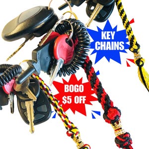 Peut inclure: Trois porte-clés tressés colorés avec des brins noirs, rouges et jaunes. Chaque porte-clés a un charme de couronne dorée avec des strass. Les porte-clés sont attachés à un jeu de clés avec un porte-clés noir et un porte-clés rétractable à ressort. L'image comprend également une étoile rouge avec le texte "BOGO 5€ DE REMISE" et une étoile bleue avec le texte "PORTE-CLÉS".