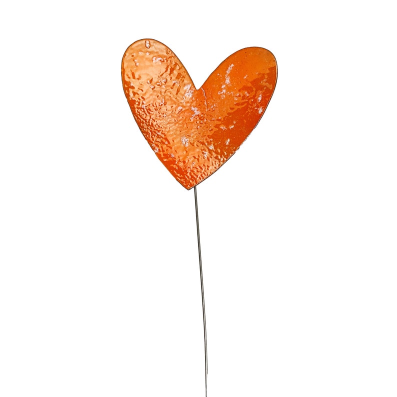 May include: An orange heart-shaped garden stake with a textured surface. The heart is mounted on a thin, dark metal rod. The stake is designed for outdoor use and adds a decorative touch to gardens.