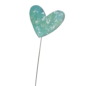 May include: A teal heart-shaped garden stake with a distressed, textured finish. The heart is mounted on a thin, dark metal rod. The stake is designed for outdoor use and adds a decorative touch to gardens and flower beds.