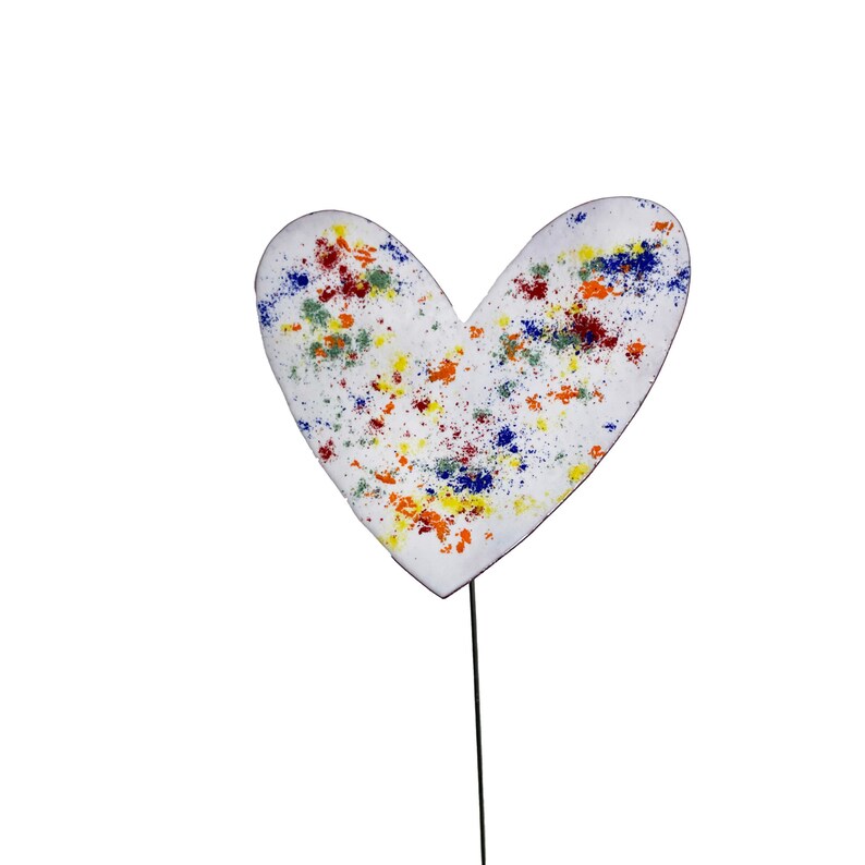 May include: A white heart-shaped garden stake with colourful paint splatters in red, yellow, blue, and green. The stake is attached to a thin, black metal rod, ideal for adding a touch of whimsy to any garden or flower pot.