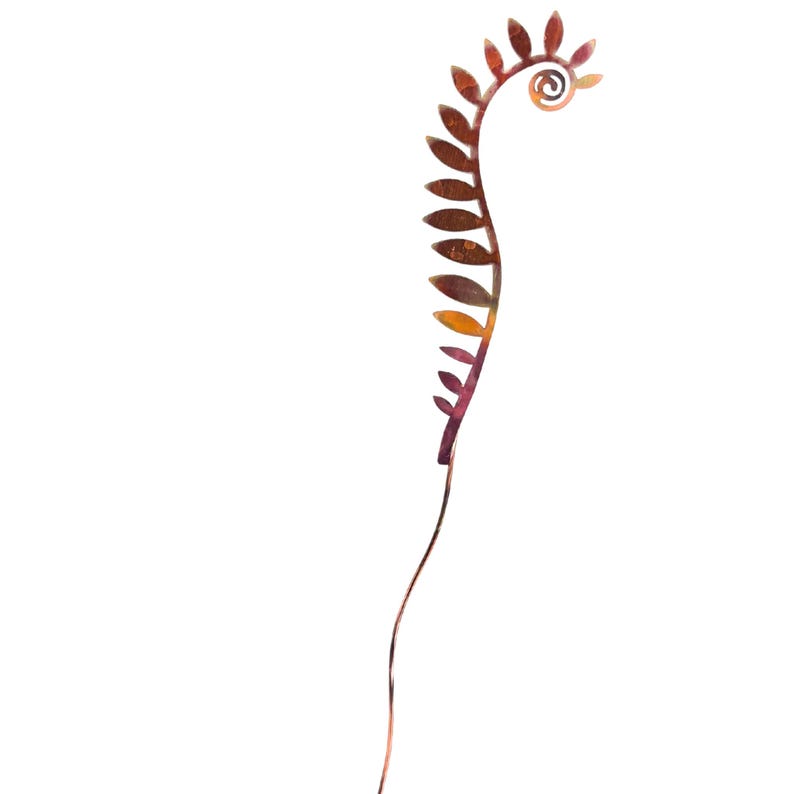 May include: A metal garden stake with a stylized fern design. The fern is made of multiple leaves in shades of orange, red, and brown. The stake is a thin, curved metal rod.