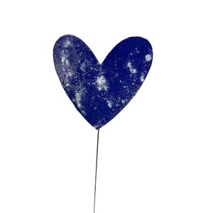 May include: A blue heart-shaped garden stake with a distressed, speckled finish. The metal heart is mounted on a thin, dark metal rod. The heart is a deep blue colour with white speckles.