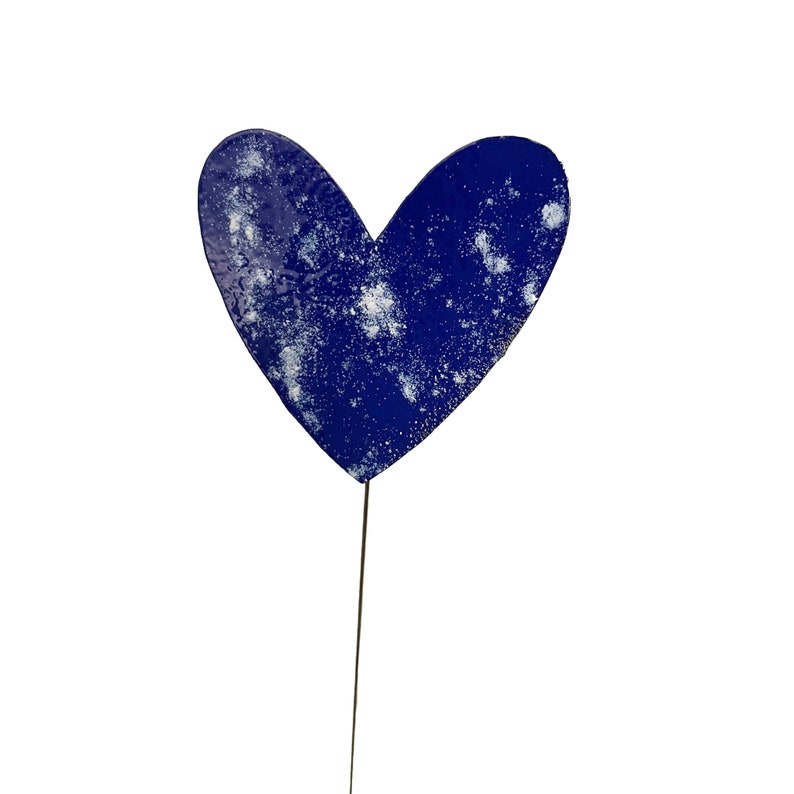 May include: A blue heart-shaped garden stake with a distressed, speckled finish. The metal heart is mounted on a thin, dark metal rod. The heart is a deep blue colour with white speckles.
