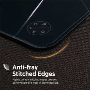 May include: A black gaming mouse pad with a white stitched border. The mouse pad has a white logo with the text "ORDA" and an arrow pointing to the right. The mouse pad is on a textured surface.