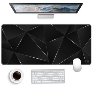 May include: A black and silver geometric design desk mat with a white wireless keyboard and mouse on a white surface.