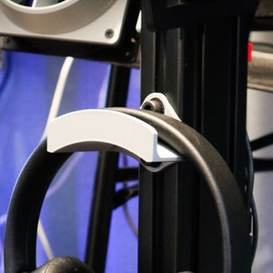 May include: A black headset with a PlayStation logo hangs on a black metal stand with a white plastic hook. The headset is hanging by the headband.