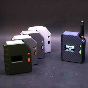 Könnte beinhalten: Eine Sammlung kleiner, rechteckiger elektronischer Geräte mit einer Kohlefaserstruktur. Die Geräte sind in verschiedenen Farben erhältlich, darunter Grün, Grau und Blau. Ein Gerät hat einen kleinen Bildschirm und eine Antenne.