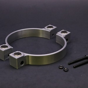 May include: Two silver metal clamps with four black square magnets on each clamp. The clamps are separated and there are two black screws and two black nuts on a black surface.