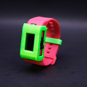 Pode incluir: Uma pulseira de rel&oacute;gio impressa em 3D de cor rosa brilhante e verde com um protetor de tela.