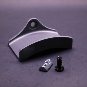 May include: A gray metal bracket with a curved shape and a hole at the top. It comes with a black screw and a silver T-nut.