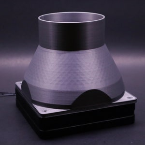 Op de afbeelding: Een 3D-geprinte grijze kunststof trechter met een vierkante basis. De trechter is bevestigd aan een zwarte en zilveren basis.