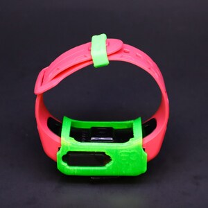 Pode incluir: Uma pulseira de pulso rosa e verde com um mostrador de rel&oacute;gio preto. A pulseira tem uma fivela verde.