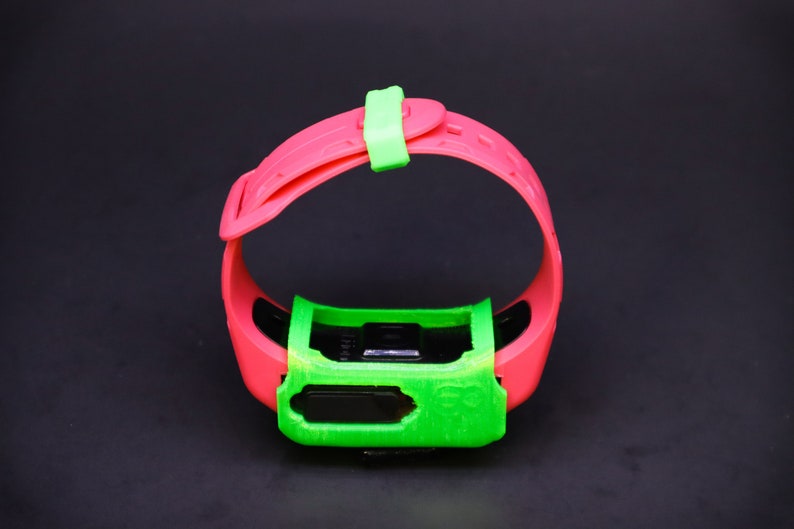 Pode incluir: Uma pulseira de pulso rosa e verde com um mostrador de rel&oacute;gio preto. A pulseira tem uma fivela verde.
