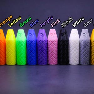 May include: A row of diamond-patterned, cylindrical objects in various colours: red, orange, yellow, green, blue, purple, pink, black, white, grey, gold, and silver. Each has a tapered top and a small logo. They are displayed against a dark background.