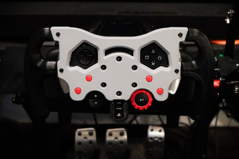 May include: A white racing steering wheel with red buttons and a black rim. The steering wheel has a variety of buttons and controls, including a red knob.